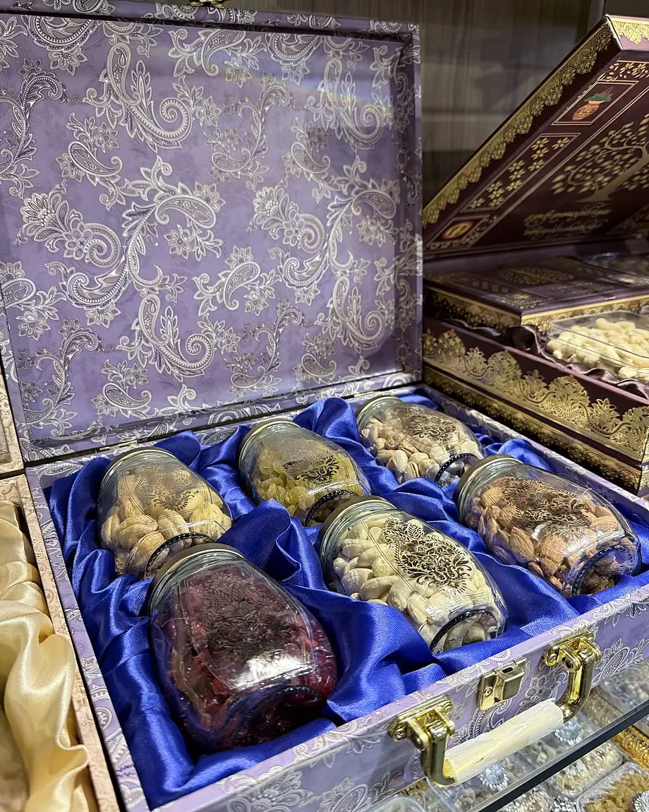 An open lilac paisley gift case with six etched glass jars of dry fruits on blue satin