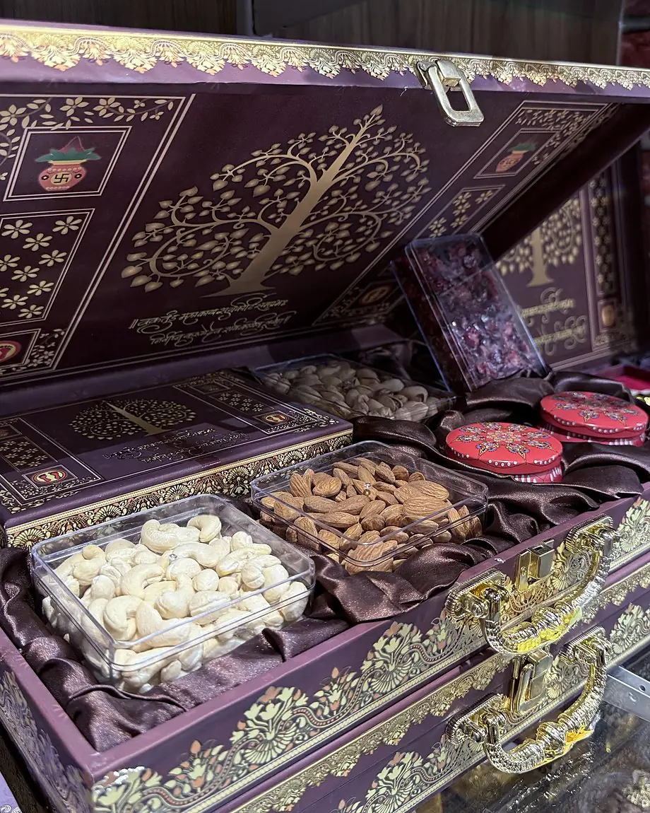 A large open plum-coloured gift case with a gold tree on the lid, holding trays of cashews and almonds and smaller boxes