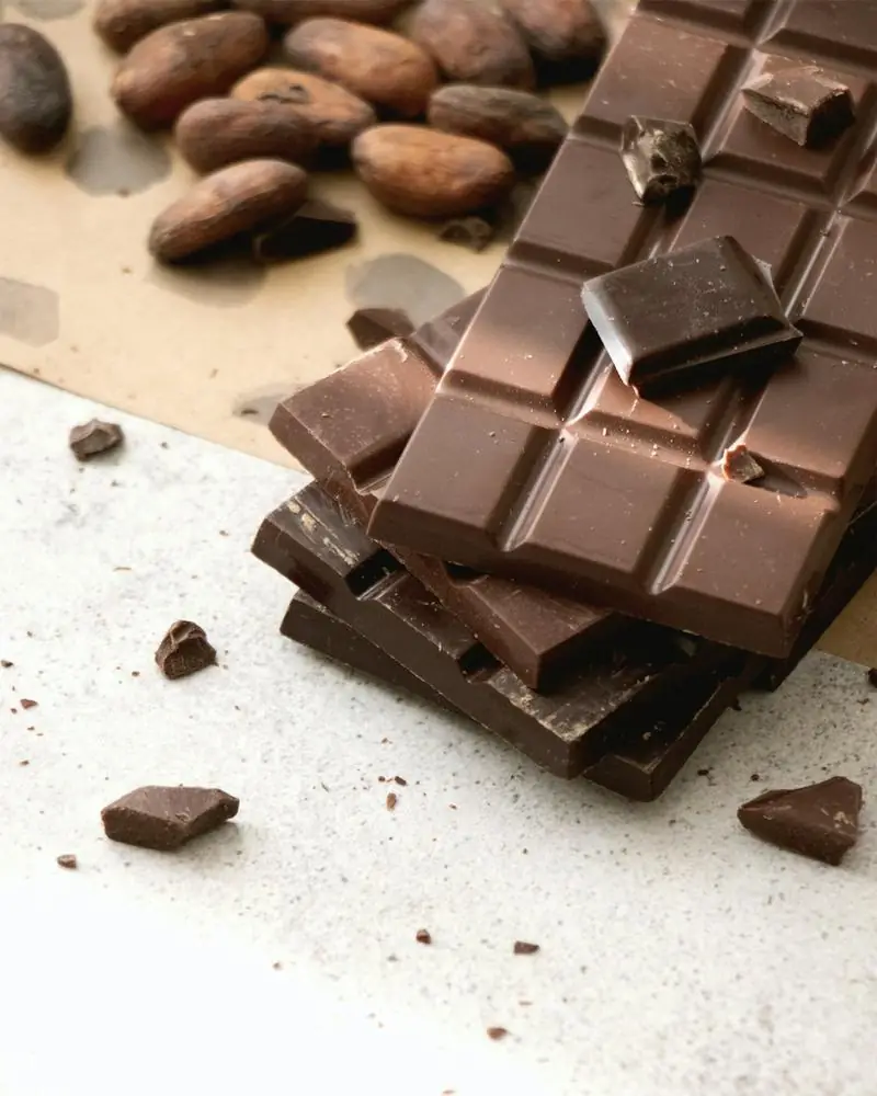 Dark chocolate bars stacked beside cocoa beans