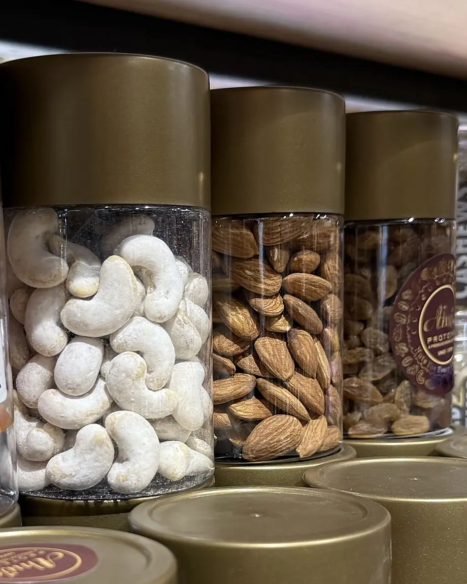 Glass jars of cashews and almonds with gold lids on a shelf at Ahuja Proteins