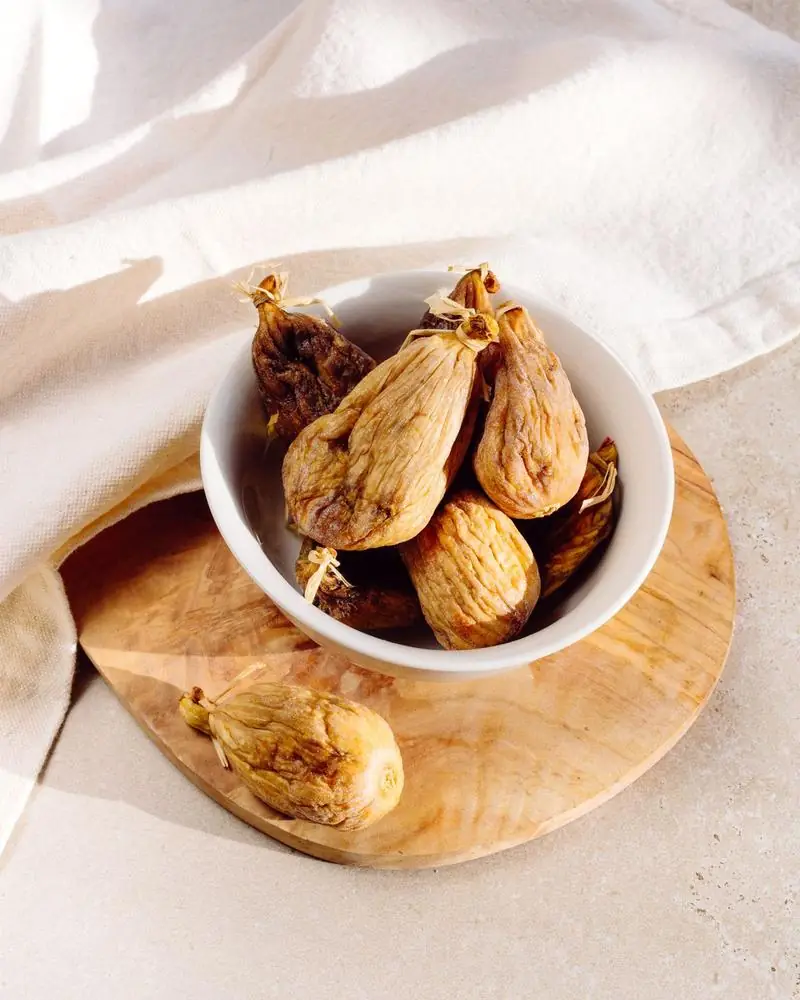 Dried figs in a white bowl on a wooden board