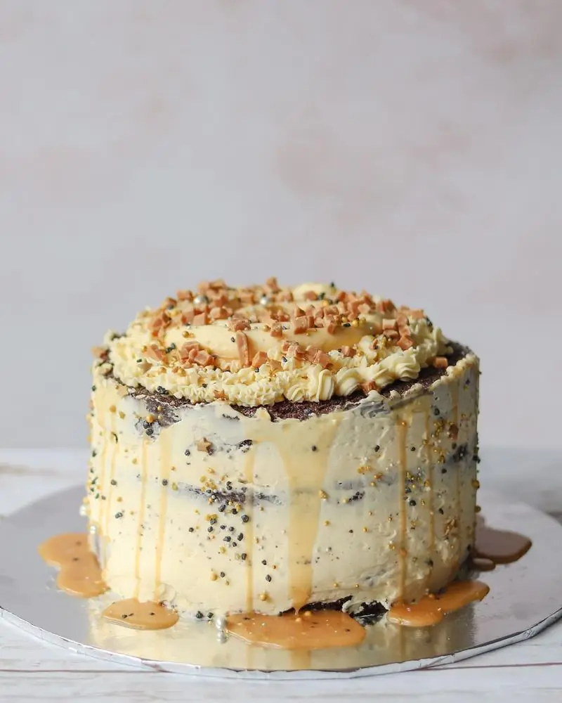 A cream-frosted layer cake with caramel drizzle and praline crumb