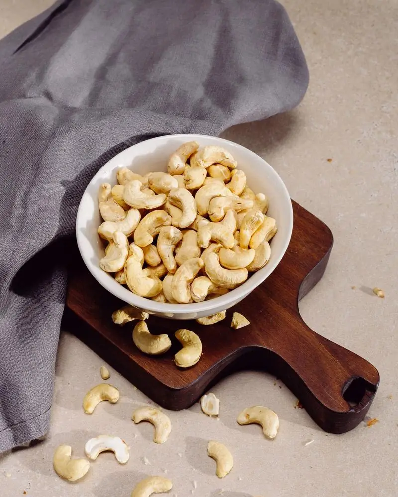 Whole cashew nuts in a bowl on a wooden board