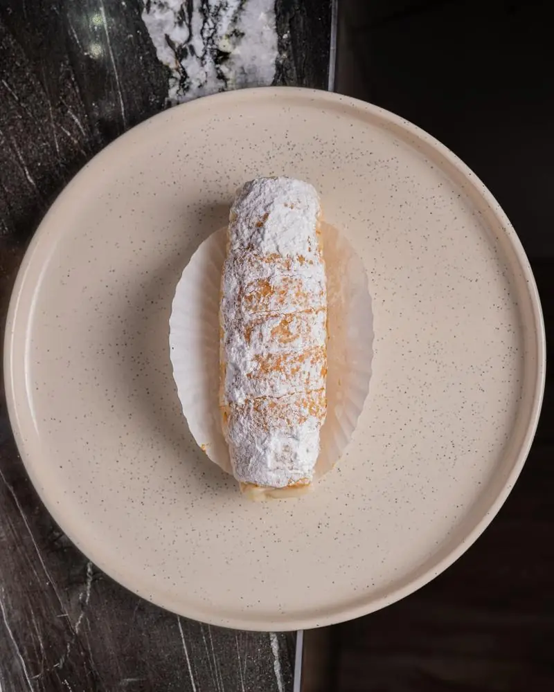 A cream-filled roll dusted with icing sugar on a plate