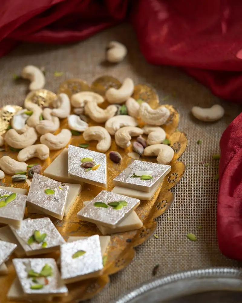 Diamonds of kaju katli with silver leaf and pistachio, cashews scattered around