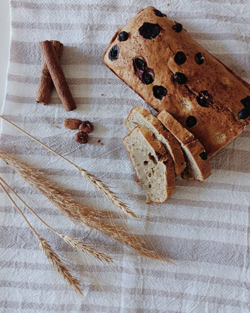 A sliced loaf cake studded with dark raisins, beside cinnamon sticks