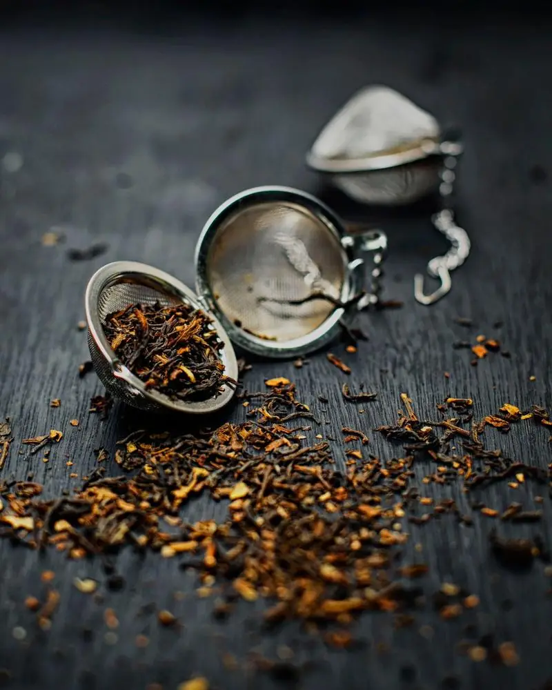 Loose black tea leaves with two metal infusers on dark wood