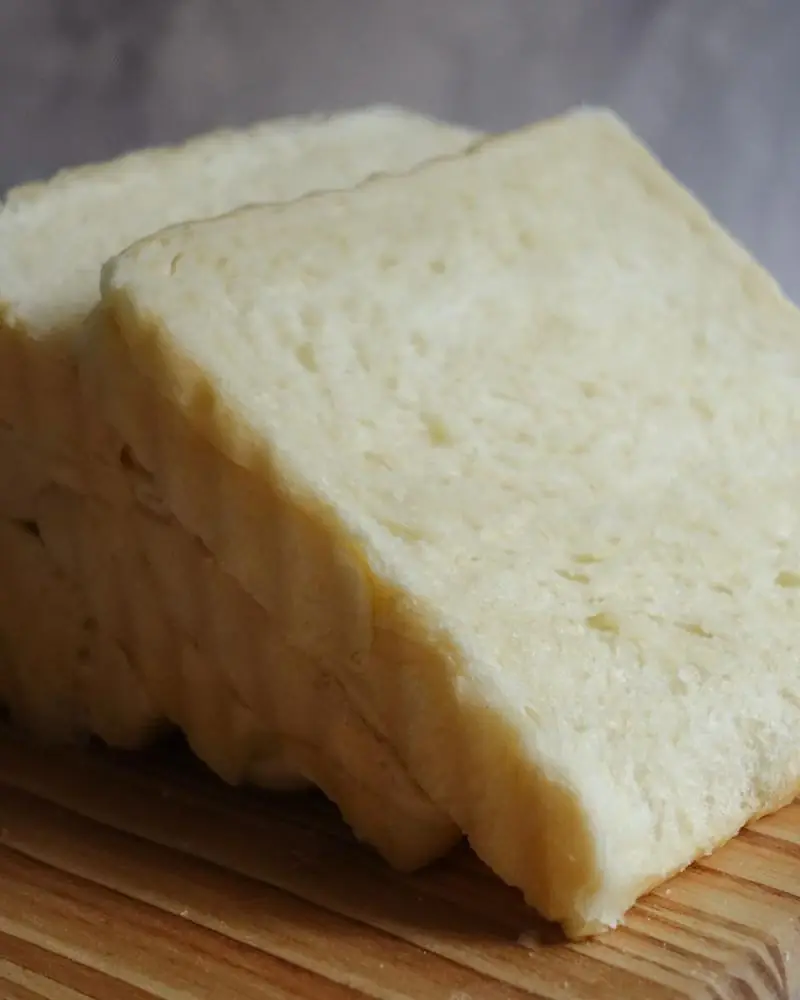 A white bread loaf, part sliced, on a wooden board